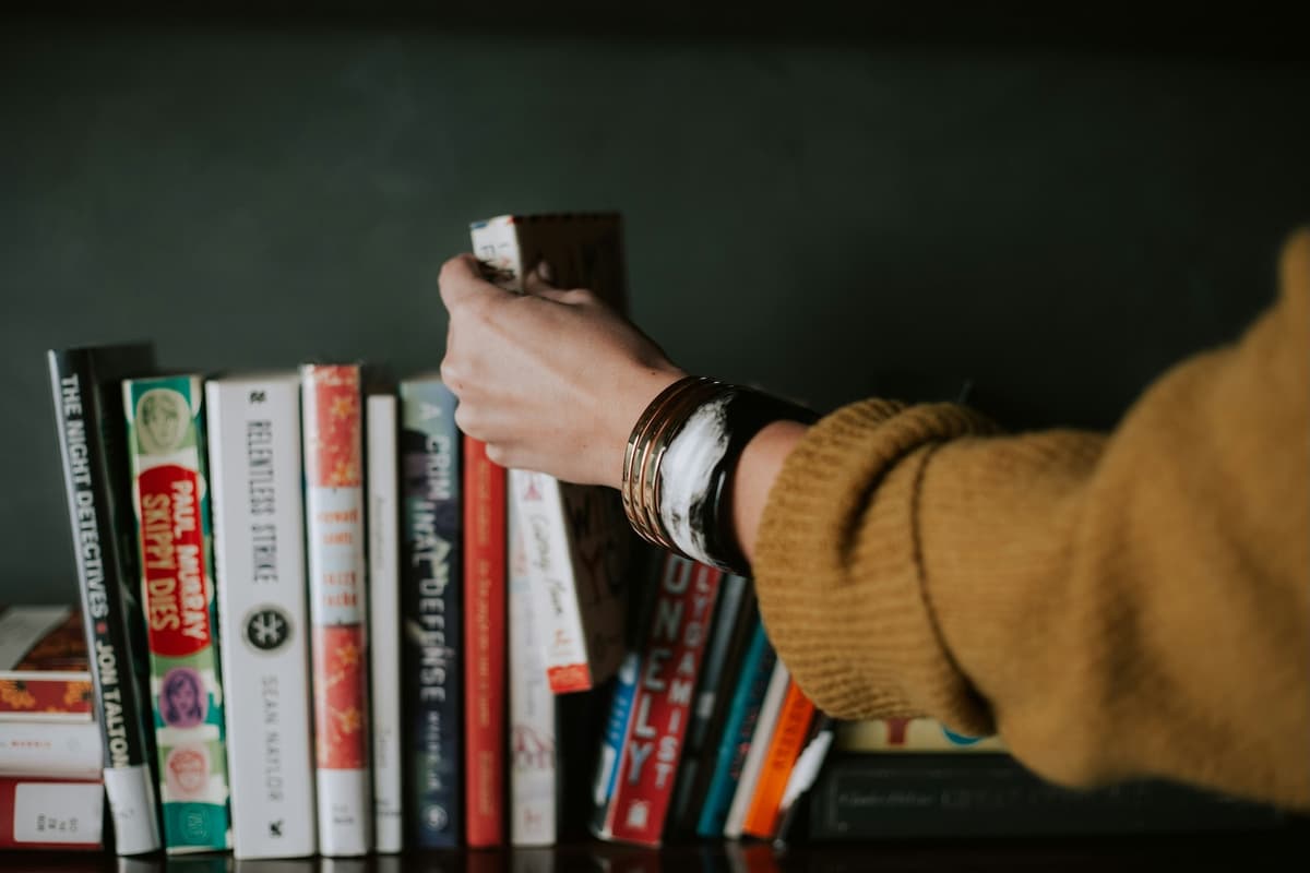 Person standing in front of a bookshelf deciding which book to pick