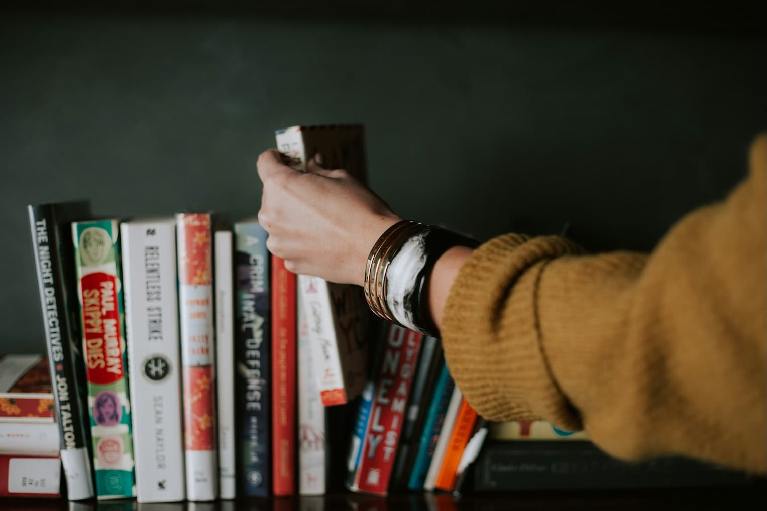 Person standing in front of a bookshelf deciding which book to pick
