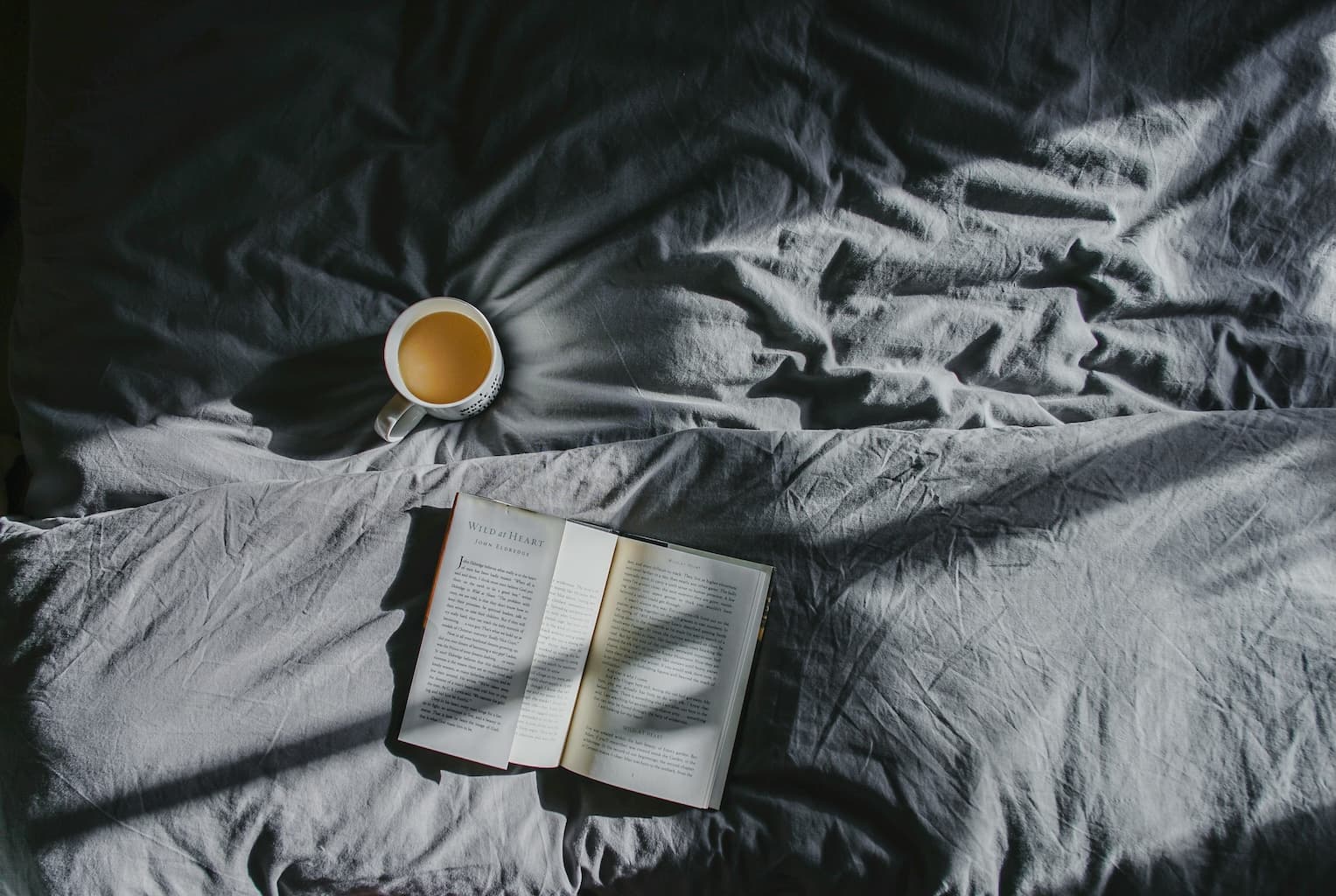 Warm morning light falling on an open book next to a coffee cup on a bed