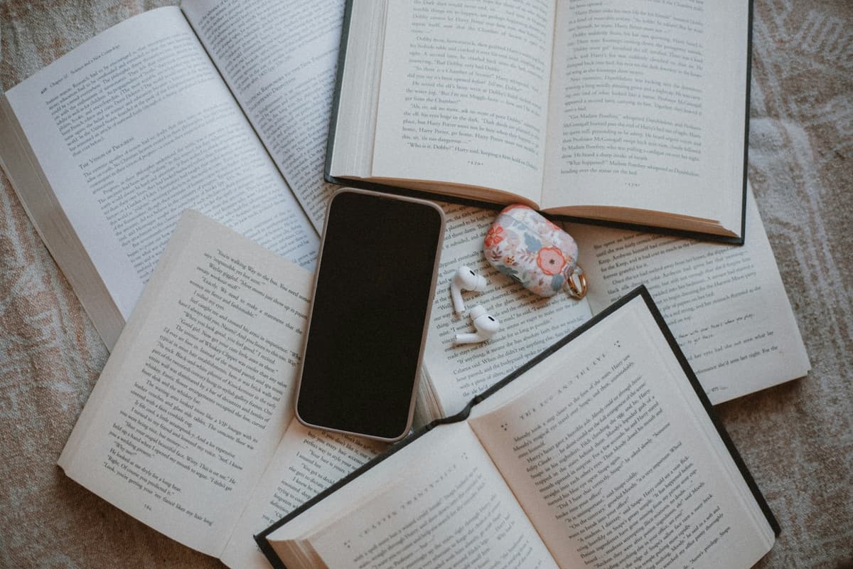Open books lying scattered on a table with a phone on top of them, representing reading distraction