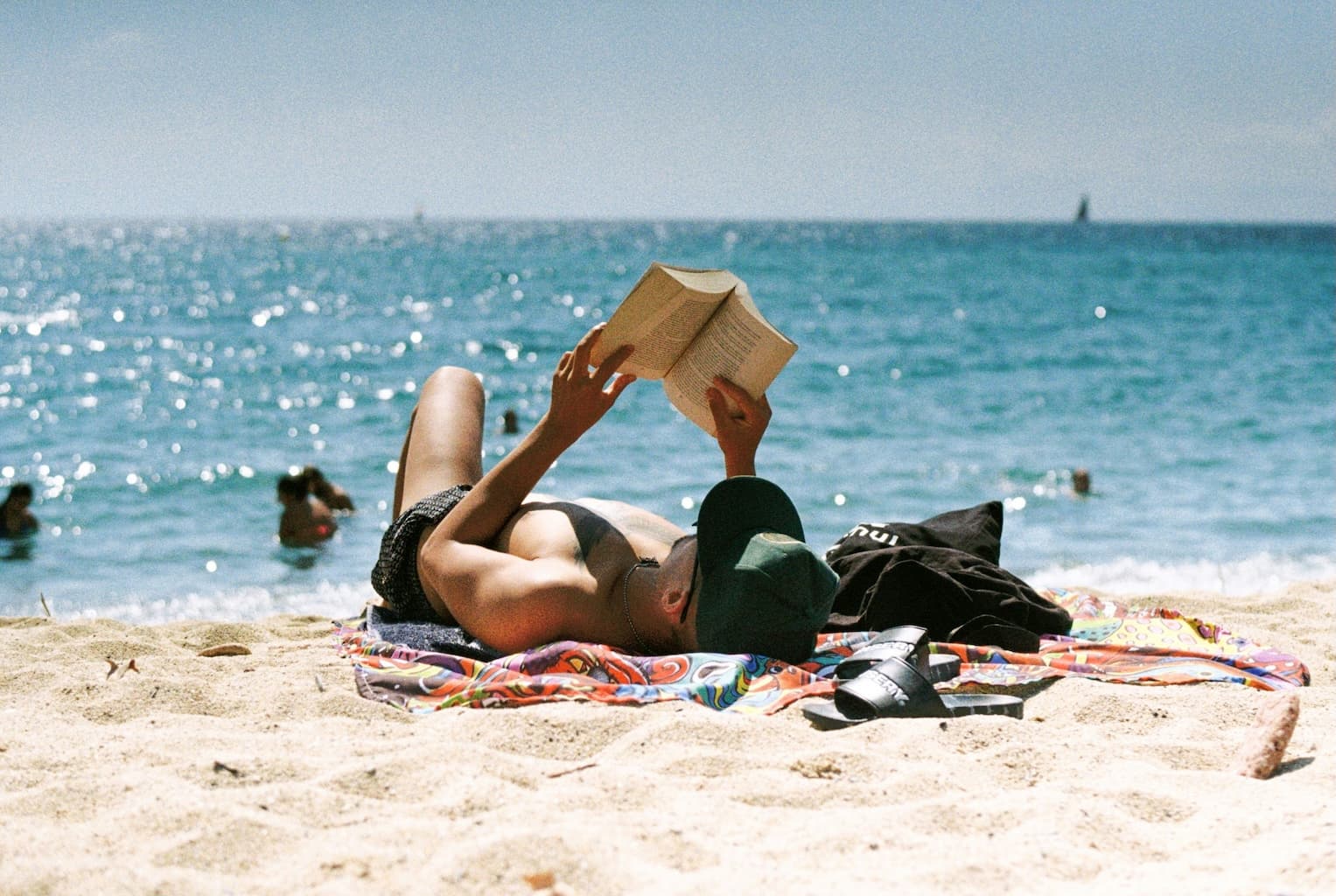 Man reading a physical book at the beach in the sun, no screens visible