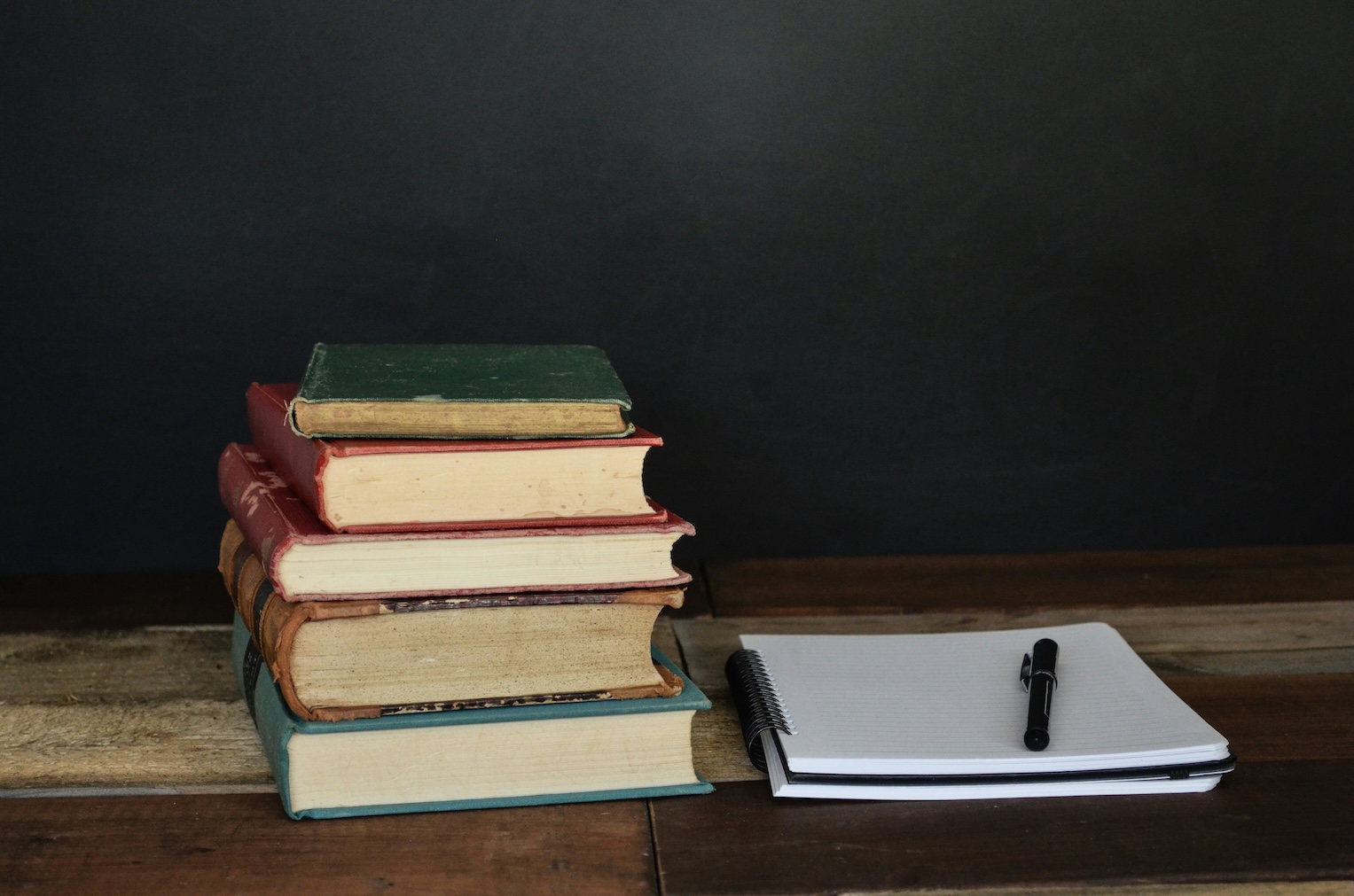 Pile of books beside a notebook with pen
