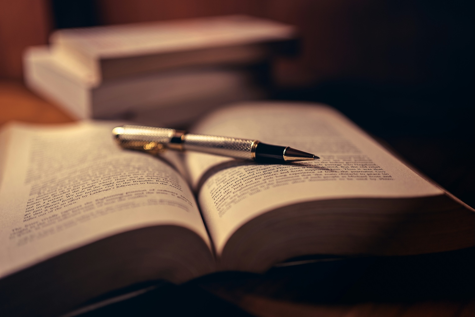 Open notebook next to a stack of books with a fountain pen resting on the page