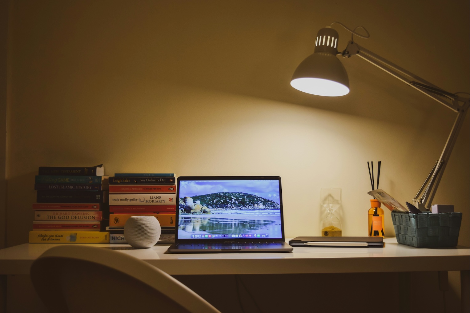 Books on a desk with an open laptop on it, end-of-workday lighting