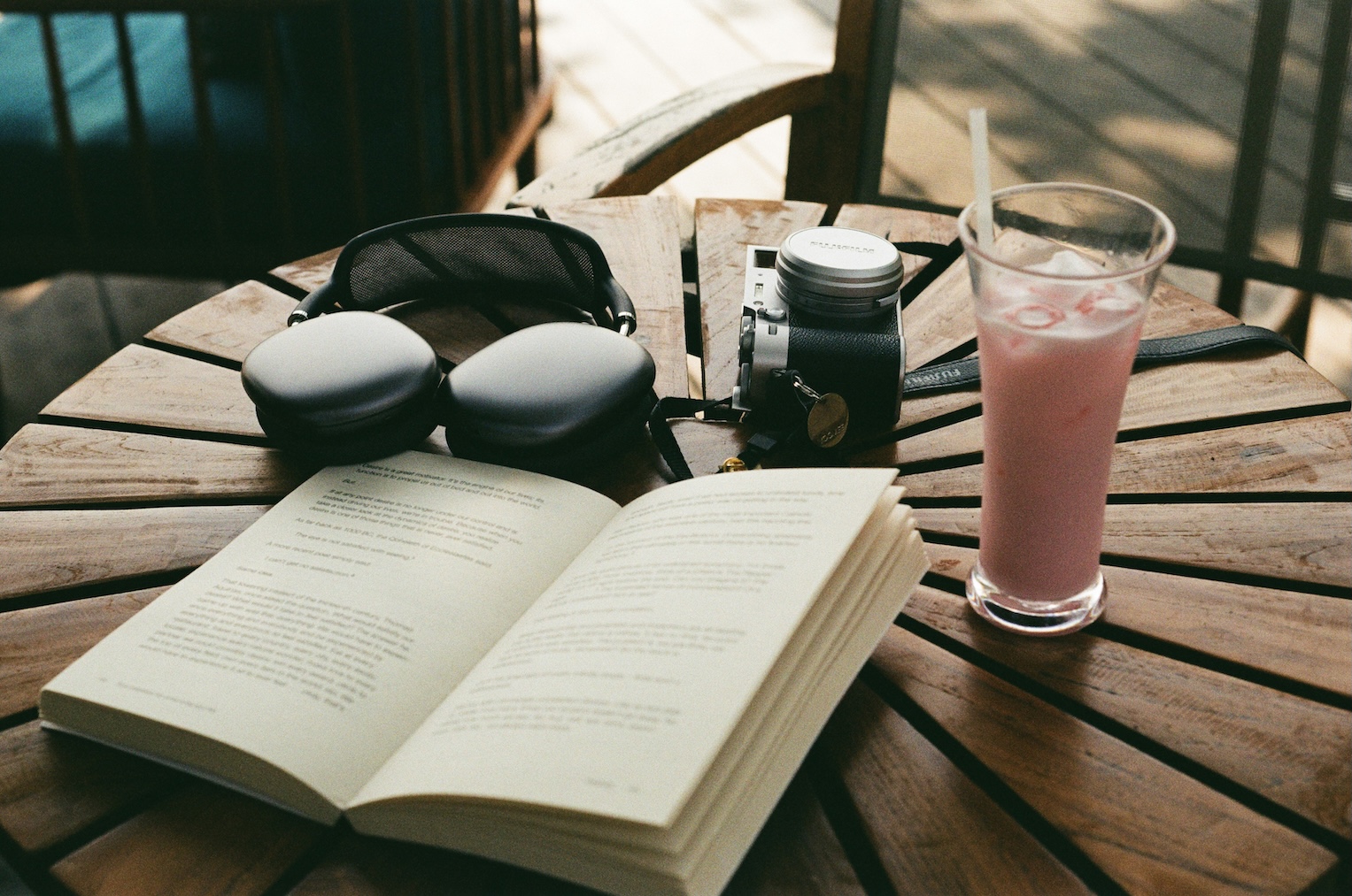 Headphones, a beverage, and an open book on a wooden table in a cafe